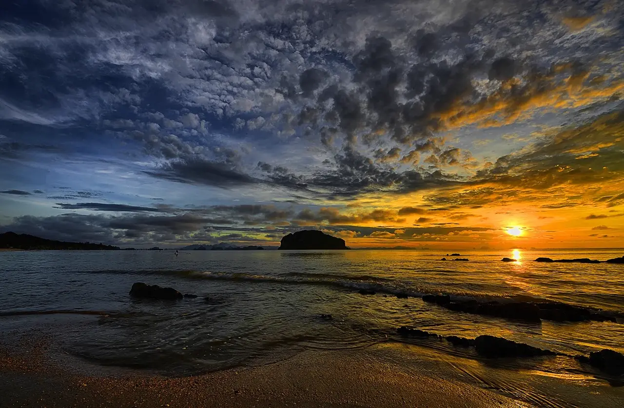 Un cielo coperto di nuvole scure che si apre verso una luce dorata sul mare: l'immagine del passaggio dal buio alla luce.